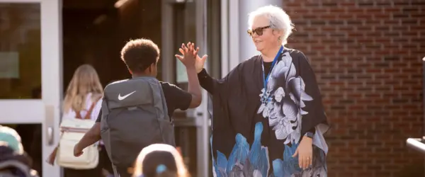 Teacher high-fiving students as they walk into school.